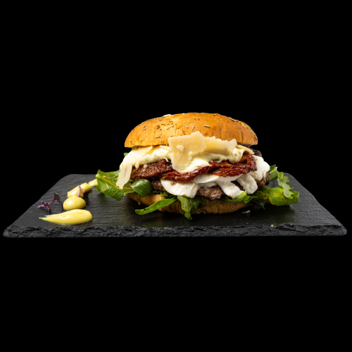 Ein Gourmet-Burger mit Salat, Tomate, geschmolzenem Käse und einer Scheibe Parmesan auf einem entkernten Brötchen, serviert auf einer schwarzen Schiefertafel mit Mayonnaise und Senf an der Seite.