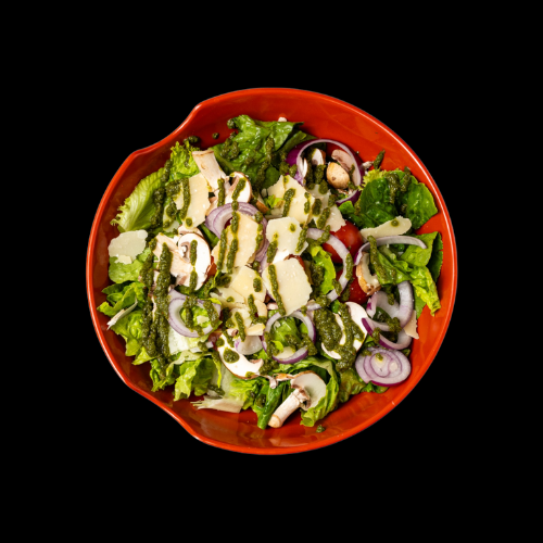 Ein frischer Salat in einer roten Schüssel mit Kopfsalat, geschnittenen roten Zwiebeln, Champignons, Tomaten, gehobeltem Käse und grünem Kräuterdressing, von oben gesehen auf schwarzem Hintergrund.